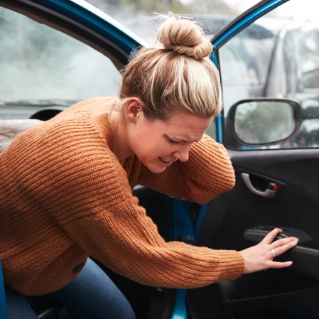 A woman holding her neck in pain as she gets out of her vehicle after an auto accident