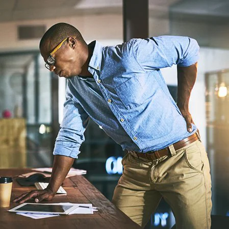 A man leaning over his desk in pain, holding his lower back